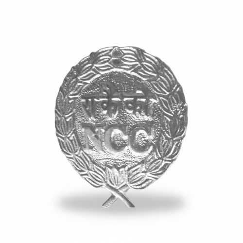 NCC aluminium metal cap badge with embossed ‘NCC’ text and wreath design, lightweight silver-tone finish, featuring crossed torch emblem and attachment loop.